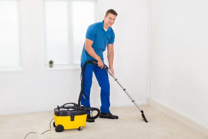 Happy Male Janitor Cleaning Carpet With Vacuum Cleaner