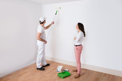 Young Housewife Looking At Painter Painting Wall In House